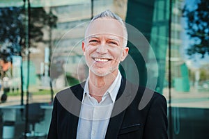 Close up portrait of mature adult business man with gray hair and suit smiling and looking at camera with succesful