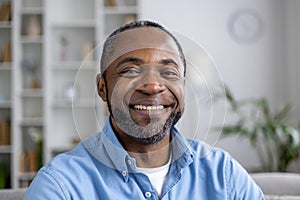 Close-up portrait of mature experienced African American man smiling and looking at camera while sitting on sofa in