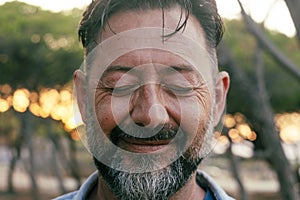 Close up portrait of mature man with beard and closed eyes smiling on camera. Wellbeing and mental health concept happiness