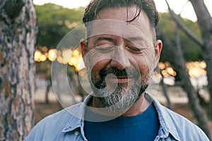 Close up portrait of mature man with beard and closed eyes smiling on camera. Wellbeing and mental health concept happiness