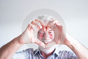 Close up and portrait of mature man and senior doing an heart with his fingers and hand in front of the camera - happy pensioner