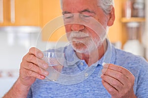 Close up and portrait of mature man or senior taking medicament and pillows with a glass of water - sick and ache pensioner