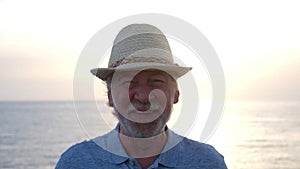 Close up and portrait of mature old man smiling and laughing looking at the camera enjoying his vacations at the beach outdoors -