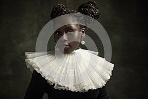 Close-up portrait of medieval African young woman in black vintage dress with big white collar posing isolated on dark