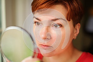 Close up portrait of Middle age woman holding round mirror and carefully looking at her reflection