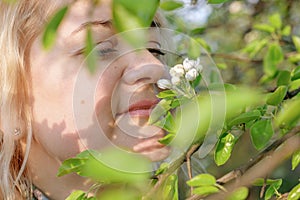 Close-up portrait of middle-aged blonde woman, woman sniffing white flowers of blooming apple tree from a tree branch