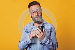 Close up portrait of middle aged Caucasian man using smarphone with shocked and surprised face expression, wearing denim jacket