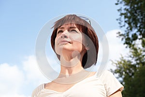 Close-up portrait of a middle-aged woman with brown hair against a blue sky