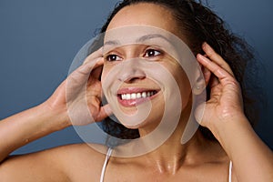 Close-up portrait of middle aged woman with no make-up and wet skin smiles toothy smile while washing her face, taking care of her