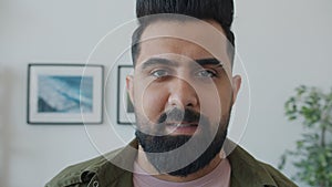 Close-up portrait of Middle Eastern man looking at camera with serious face then smiling at home