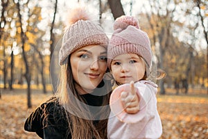 Close up portrait of mom and toddler baby daughter in autumn park with baby stroller. Happy family mom and toddler