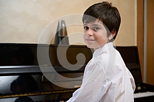 Close-up portrait of a multi ethnic teen boy, little pianist musician smiling looking at camera, sitting at piano forte