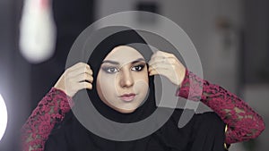 Close-up portrait of a muslim woman in national clothes adjusting her hijab while looking in the mirror. Slow motion