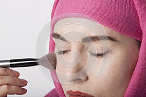 Close-up portrait of a muslim woman wearing a head scarf and doing make-up. Isolated.