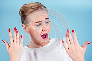 Close-up portrait of nervous unhappy young blonde woman looking at a broken fingernail and crying . red long nails