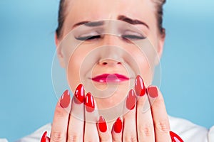 Close-up portrait of nervous unhappy young blonde woman looking at a broken fingernail and crying . red long nails