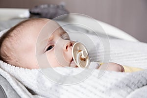 A close-up portrait of a newborn baby girl, who lies in a cradle and sucks a pacifier