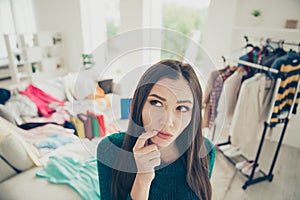 Close-up portrait of nice attractive charming pensive uncertain girl among different clothes making choice what to put