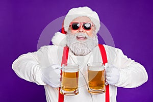 Close-up portrait of nice glad cheerful cheery positive bearded Santa holding in hands two mugs drinking beer having fun