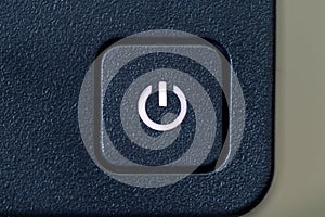 A close up portrait of an on or off button of a PC screen. The computor monitor is turned on because the light in the symbol of
