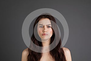 Close up portrait of offended unhappy beautiful woman with long brunette hair, bare shoulders