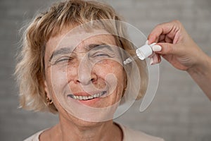 Close-up portrait of an old woman applying hyaluronic acid serum with a pipette. Anti-aging face care.