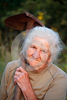 Close-up portrait of an old woman with gray hair smiling and looking at the camera, holding a rusty shovel in her hands, face in