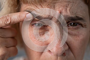 Close-up portrait of an old woman pointing at a wrinkle on her upper eyelid.