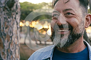 Close up portrait outdoor of adult mature man with beard and big smile looking at the park. Aged male person in cheerful