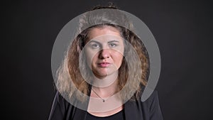 Close-up portrait of overweight caucasian woman approvingly nodding into camera on black background.