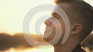 Close up portrait of pensive handsome young man looking up enjoying nature in sun rays at sunset