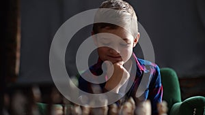 Close-up portrait of pensive little boy thinking about next move over the chessboard sitting at desk