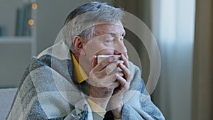 Close up portrait of pensive mature old man wrapped in warm blanket drinking hot tea calm grandfather resting alone