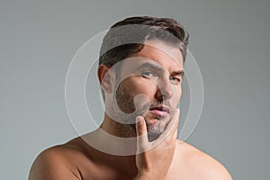 Close-up portrait of perfect brunet man touching chin and skin. Handsome man touching face in gray studio isolated