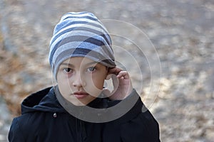 Close-up portrait of a poor child with hearing problems, holding his hand near his ear, showing me that he does not hear