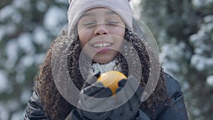 Close-up portrait of positive cute teenage girl smelling healthful vitamin orange standing in winter forest. Happy