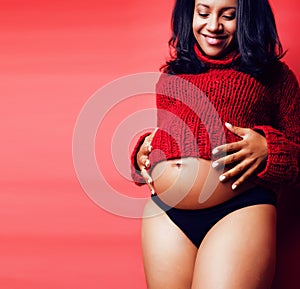 close up portrait of pregnant woman with big belly, hands hold, red sweater on background, choise of gender, lifestyle