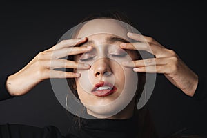 Close up portrait of pretty beautiful young woman wearing black sweater isolate over dark background. Two hands on face posing