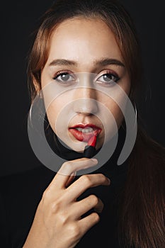 Close up portrait of pretty beautiful young woman wearing black sweater isolate over dark background. Woman using red lipstick.