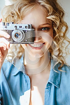 Close up portrait of pretty blonde young woman with old vintage camera in her hands