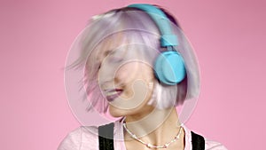 Close-up portrait of pretty girl with dyed violet hair listening to music, smiling, dancing in headphones in studio