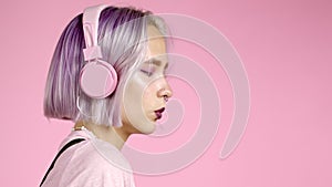 Close-up portrait of pretty girl with dyed violet hair listening to music, smiling, dancing in headphones in studio