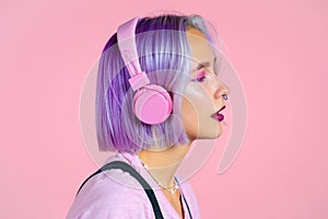 Close-up portrait of pretty girl with dyed violet hair listening to music, smiling, dancing in headphones in studio