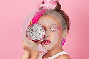 Close-up portrait of pretty girl with pink hairstyle with dragon fruit on pink background. Studio shot of charming tween