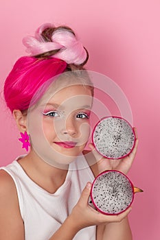 Close-up portrait of pretty girl with pink hairstyle with dragon fruit on pink background. Studio shot of charming tween