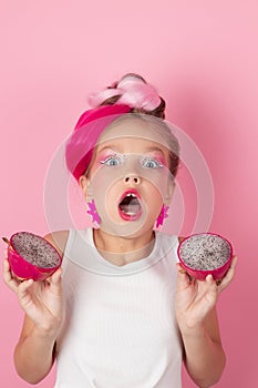 Close-up portrait of pretty girl with pink hairstyle with dragon fruit on pink background. Studio shot of charming tween