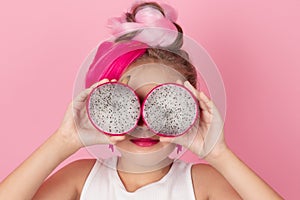 Close-up portrait of pretty girl with pink hairstyle with dragon fruit on pink background. Studio shot of charming tween