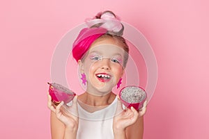 Close-up portrait of pretty girl with pink hairstyle with dragon fruit on pink background. Studio shot of charming tween