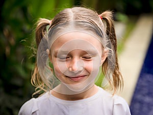 Close up portrait of pretty little girl. Face with closed eyes. Caucasian girl with two ponytails. Green tropical leaves and