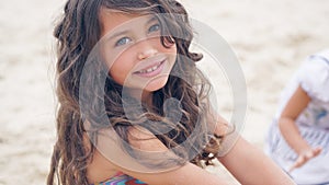 Close-up portrait of a pretty little Hispanic girl with waving in the wind long hair sitting on the beach.